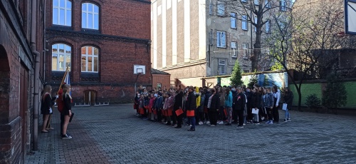 Uczniowie stoją na podwórzu szkolnym i w obecności sztandaru śpiewają hymn szkoły